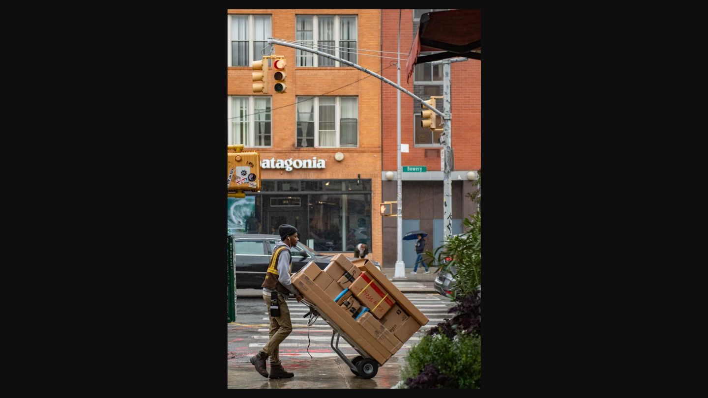Courier pushing a hand truck with packages across a rainy city street